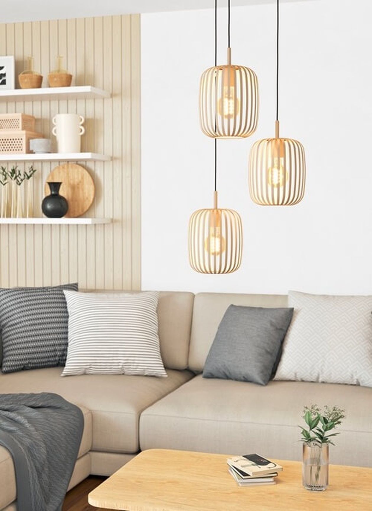 Modernes Wohnzimmer mit beigem Sofa, grauen und gestreiften Kissen, einem Couchtisch aus Holz und drei Pendelleuchten. Dekorierte Regale an der Wand.