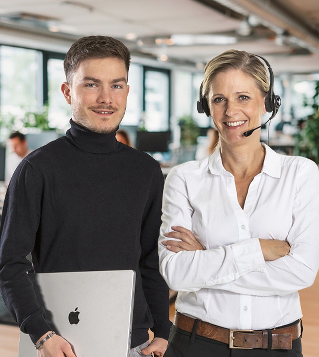 Eine Frau mit Headset und ein junger Mann mit Laptop arbeiten freundlich im Büro, möglicherweise im Kundenservice oder IT-Support.