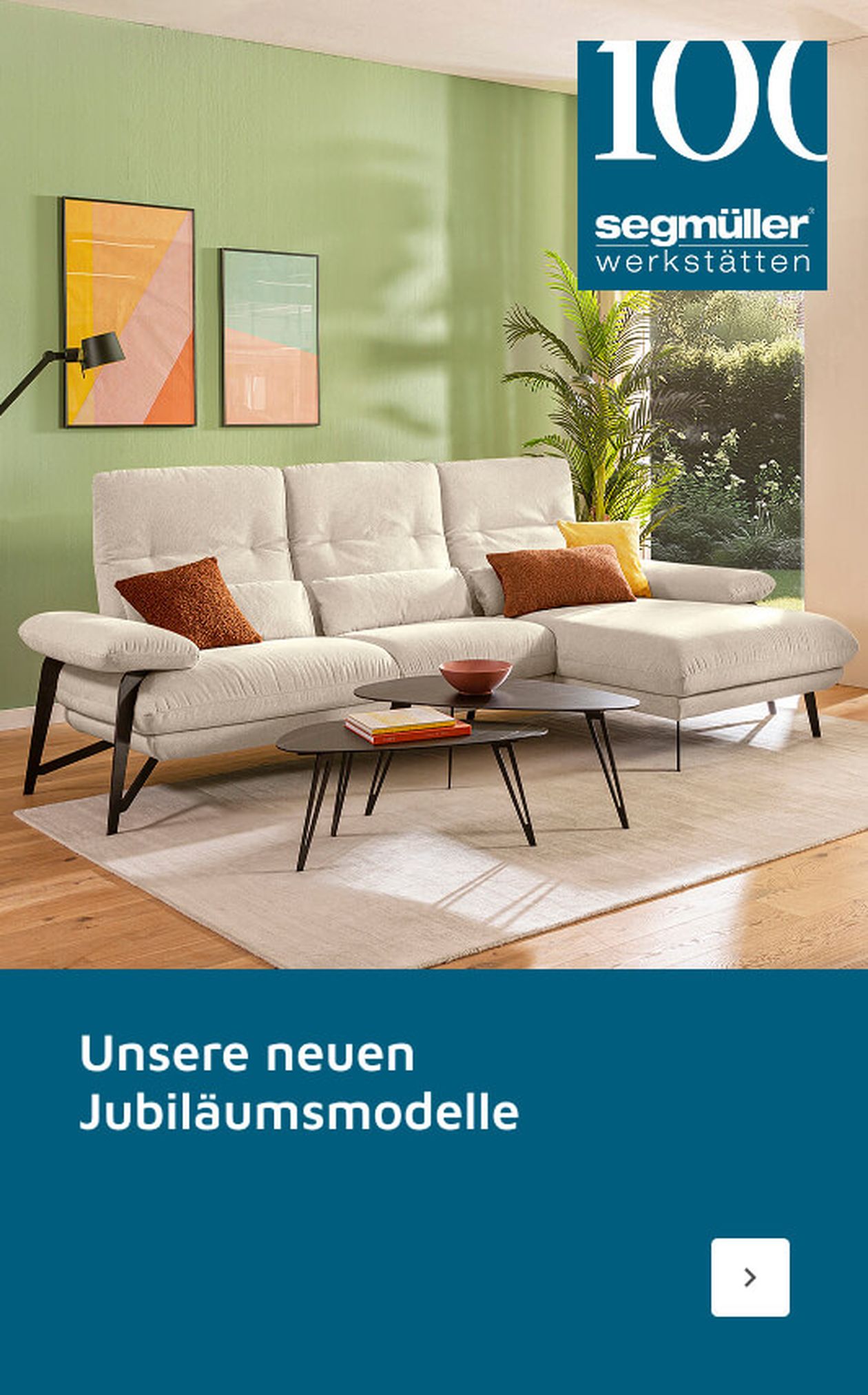 Modernes Wohnzimmer mit weißem Sofa, bunten Kissen, runden Couchtischen und abstrakter Wandkunst. Text: „Unsere neuen Jubiläumsmodelle.“