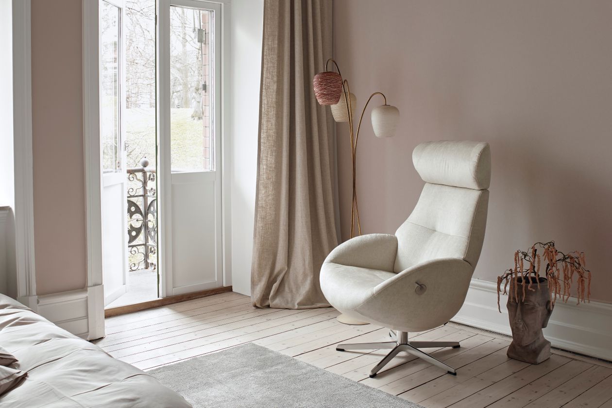 Auf dem Foto befindet sich ein cremefarbener Relaxsessel mit Kopfstütze. Der Raum ist schlicht eingerichtet mit rosa Wänden und weißen Akzenten.