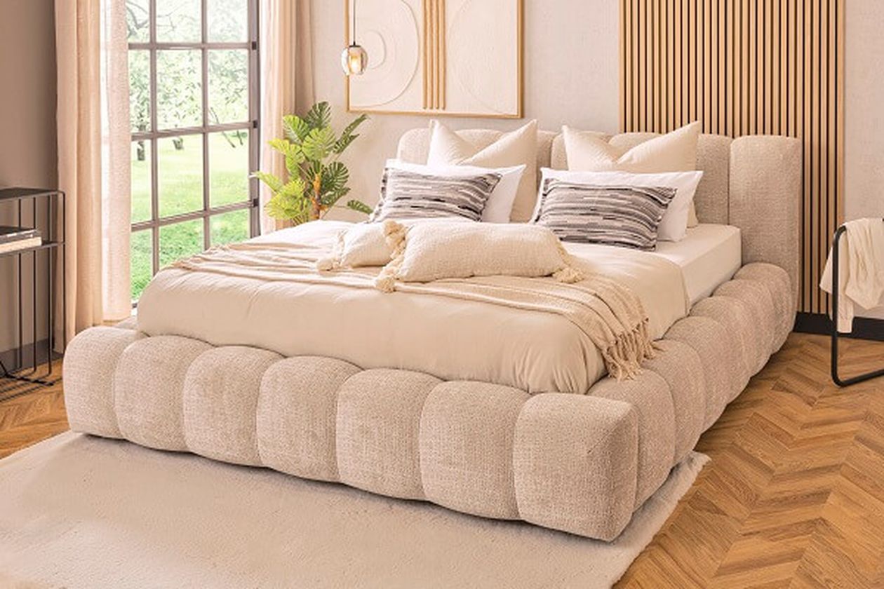 Großes, beiges Polsterbett in einem hellen, gemütlichen Schlafzimmer.