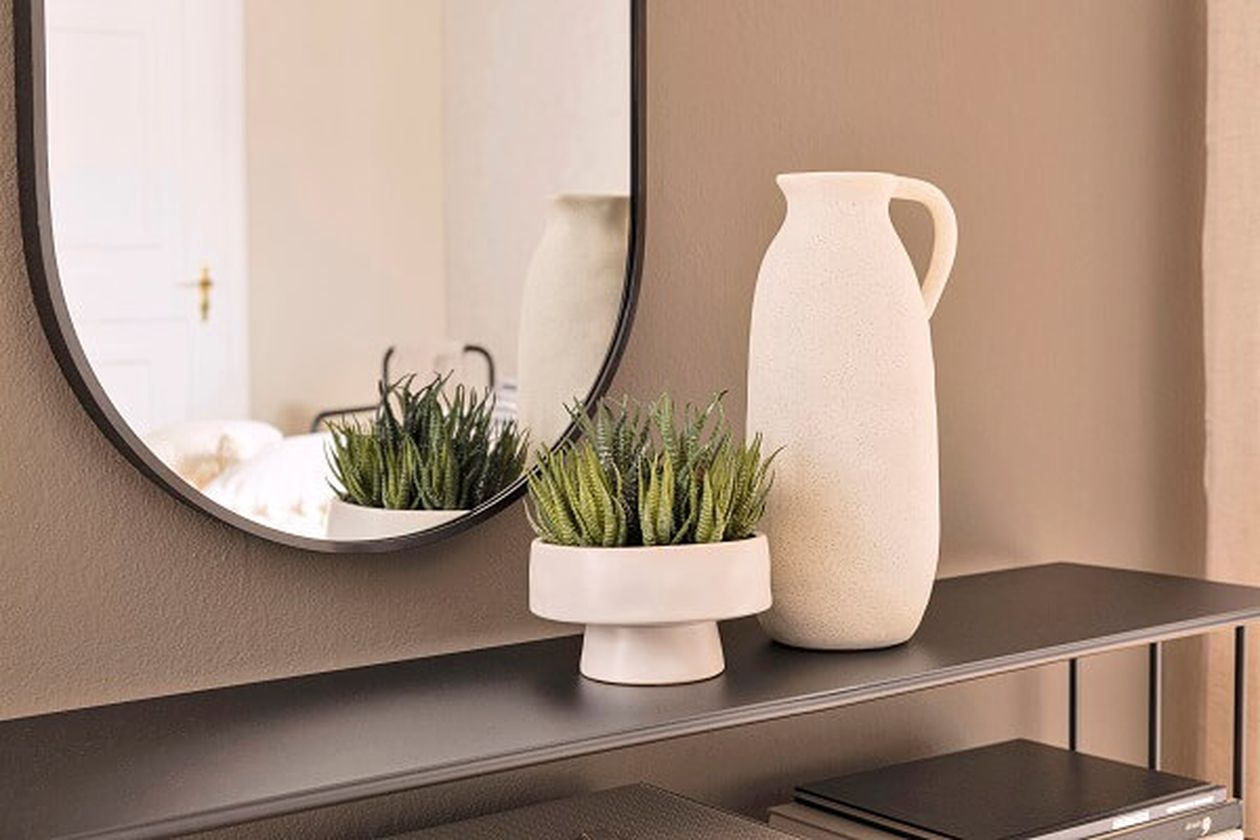 Krugförmige, beige Vase und eine Sukkulente auf einem schwarzen Sideboard.