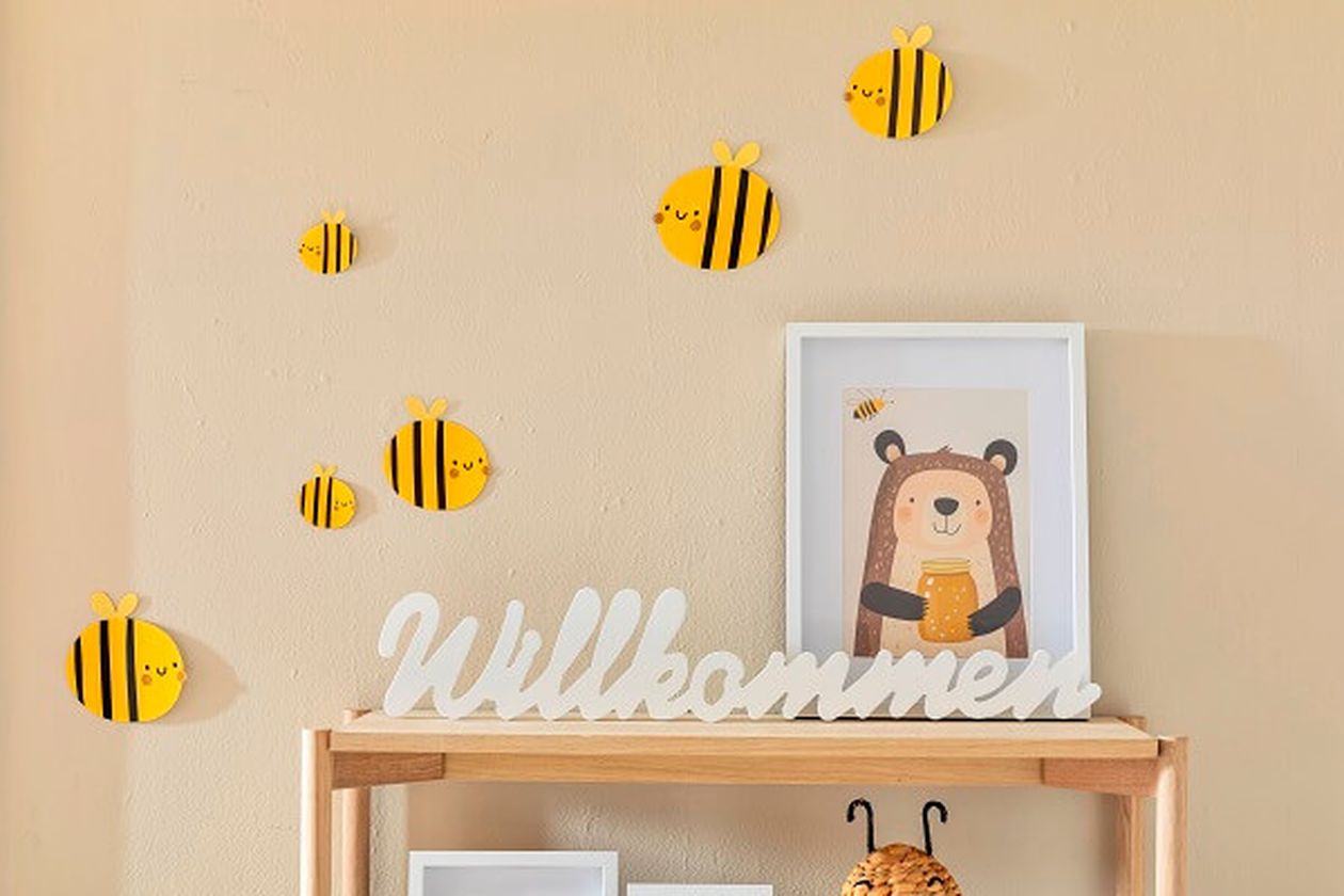 Papier-Bienen an einer beigen Wand neben einem Bücherregal mit kindlicher Deko.