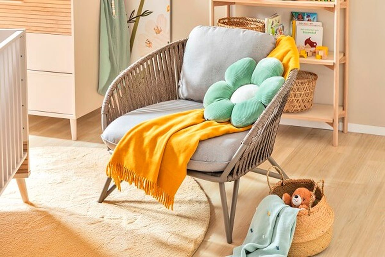 Gemütlicher Lesesessel in einem freundlich gestalteten Babyzimmer mit gelber Kuscheldecke und grünem Kissen in Blumenform.