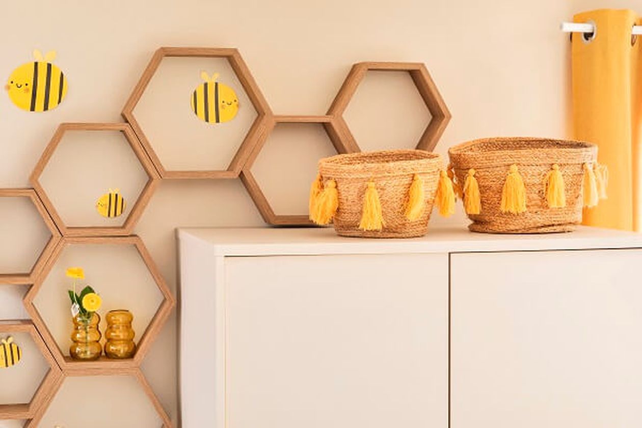 Obere Ecke eines hellen Kleiderschranks mit Körben aus Geflecht und hölzernen, wabenförmigen Wandregalen.