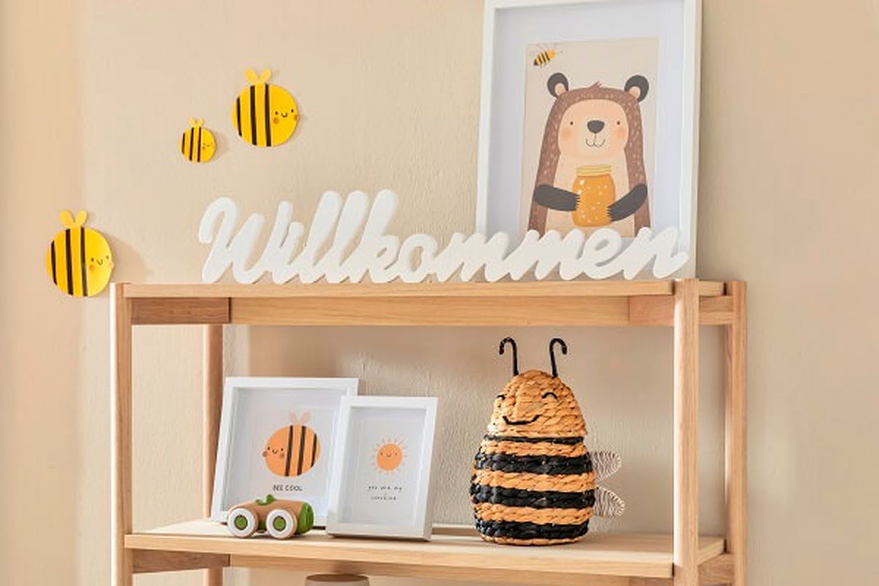 Bücherregal aus hellem Holz mit kindlichen Bienchen-Motiven als Dekoration.