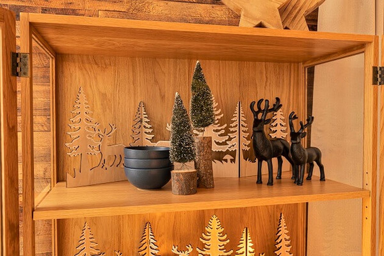 Holzregal mit dekorativen Bäumen, blauen Schalen und schwarzen Rentierfiguren vor einem geschnitzten Waldhintergrund.
