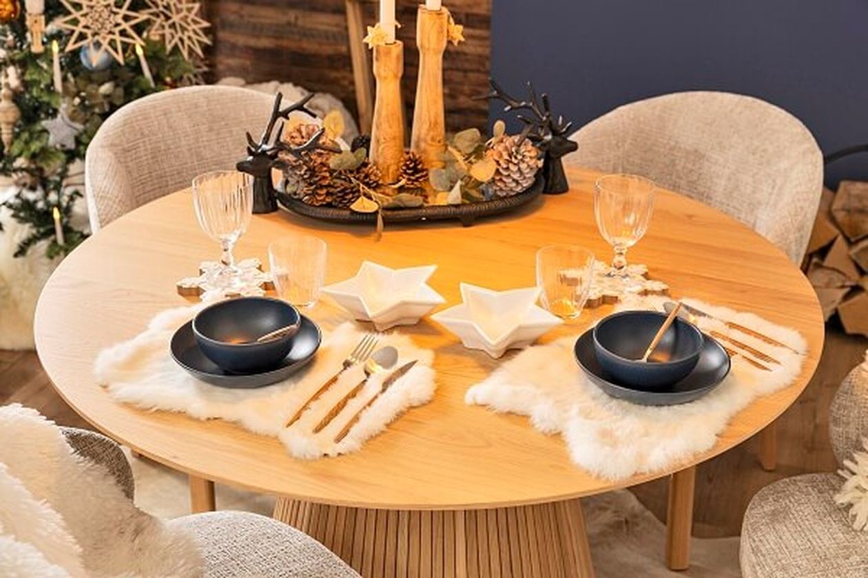 Festliche Tischdekoration mit sternförmigen Tellern, schwarzen Schüsseln und goldenem Besteck auf einem Holztisch, geschmückt mit Kerzen und Tannenzapfen.