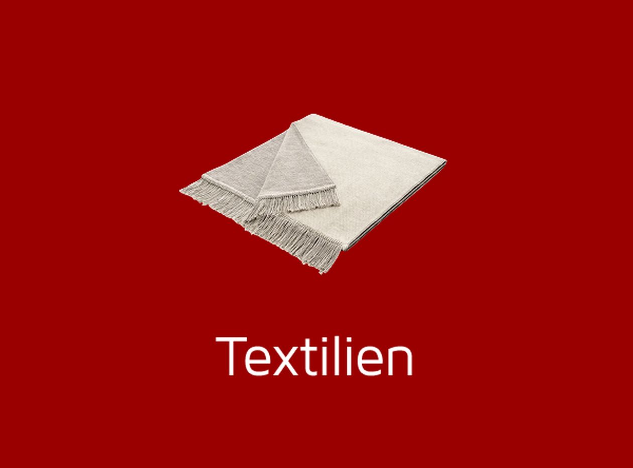 Zwei gefaltete Decken mit Fransen auf rotem Hintergrund, darunter steht "Textilien".