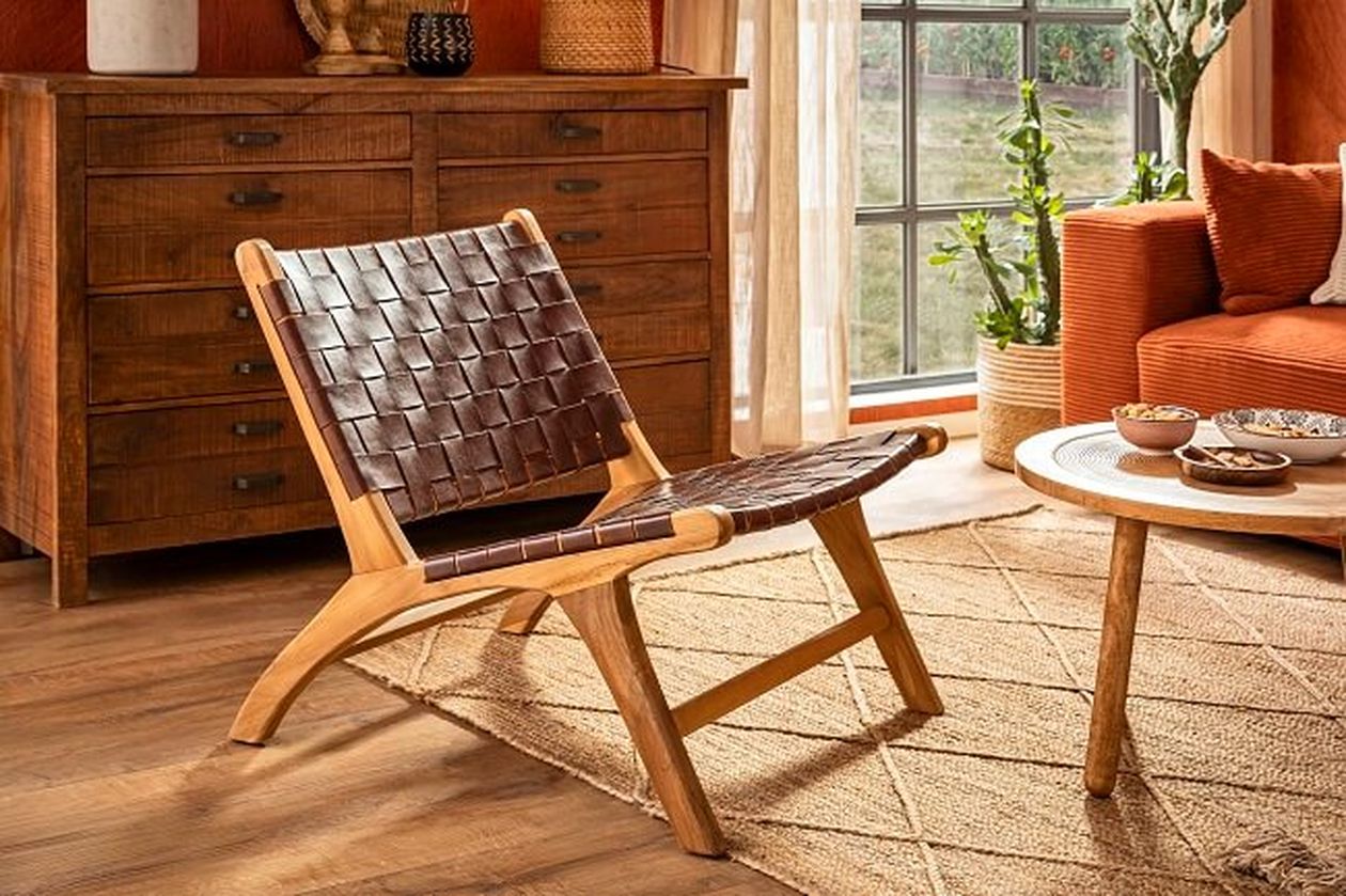 Modernes Wohnzimmer mit einem gewebten Ledersessel, einer Holzkommode, einem orangefarbenen Sofa und einem runden Couchtisch auf einem gemusterten Teppich in der Nähe eines Fensters.