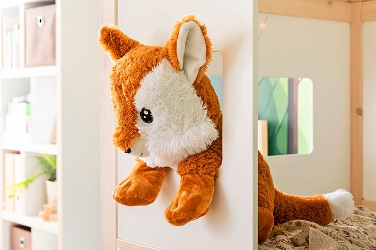 In einem gemütlichen Zimmer liegt ein Plüschfuchs mit weißem und orangefarbenem Fell über einem weißen Hochbett.