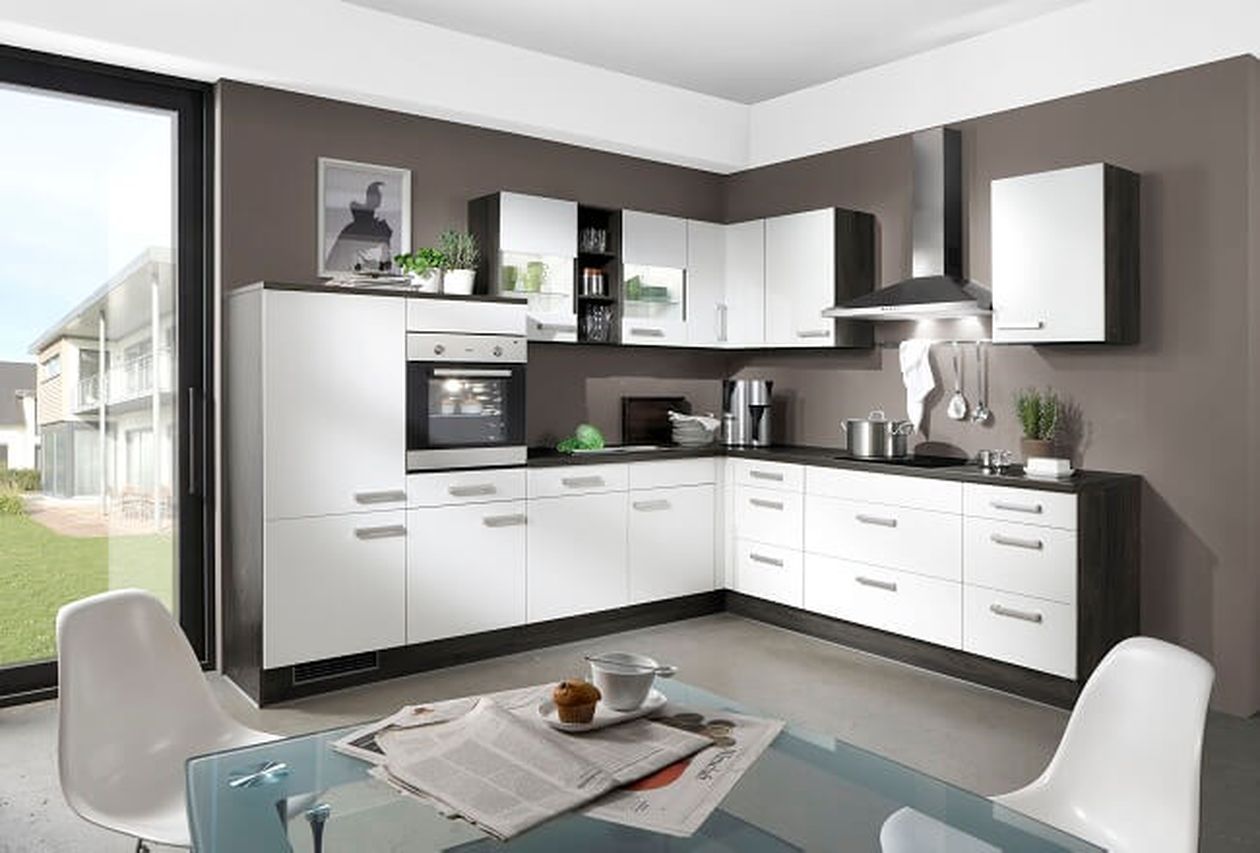 Moderne Küche mit weißen Schränken, Glastisch, Stühlen, Zeitung und Kaffeetasse. Großer Fensterblick auf Rasen und Gebäude im Hintergrund.