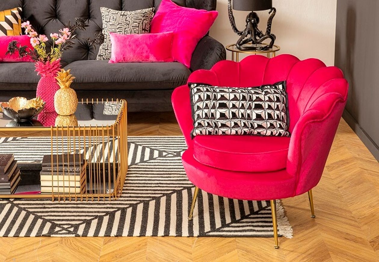 Lebendiges Zimmer mit einem pinkfarbenen Sessel, einem gemusterten Kissen, einem dunklen Sofa, einem geometrischen Teppich und einem Tisch mit Büchern und Dekorationsgegenständen.