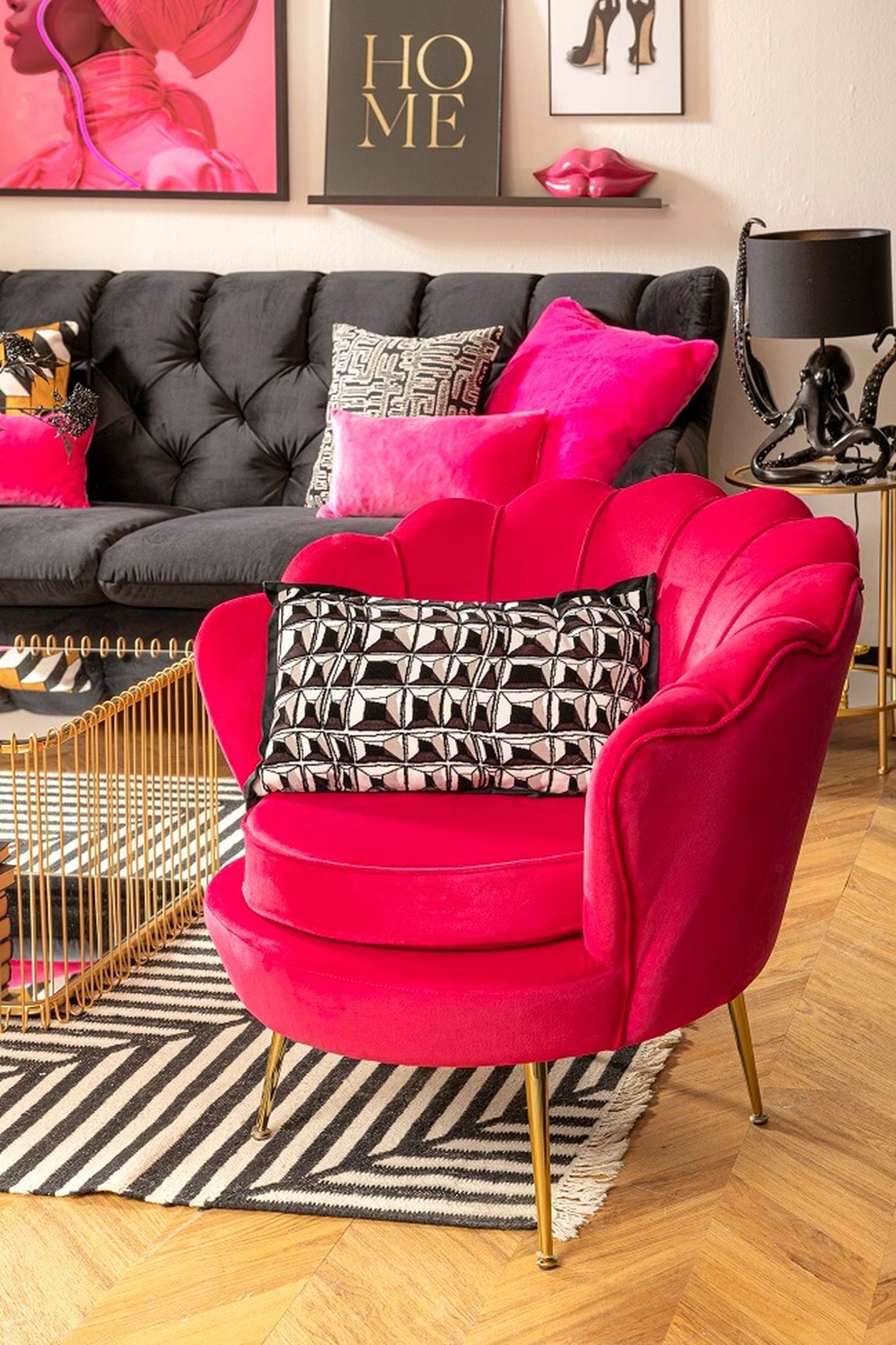 Lebendiges Zimmer mit einem pinkfarbenen Sessel, einem gemusterten Kissen, einem dunklen Sofa, einem geometrischen Teppich und einem Tisch mit Büchern und Dekorationsgegenständen.