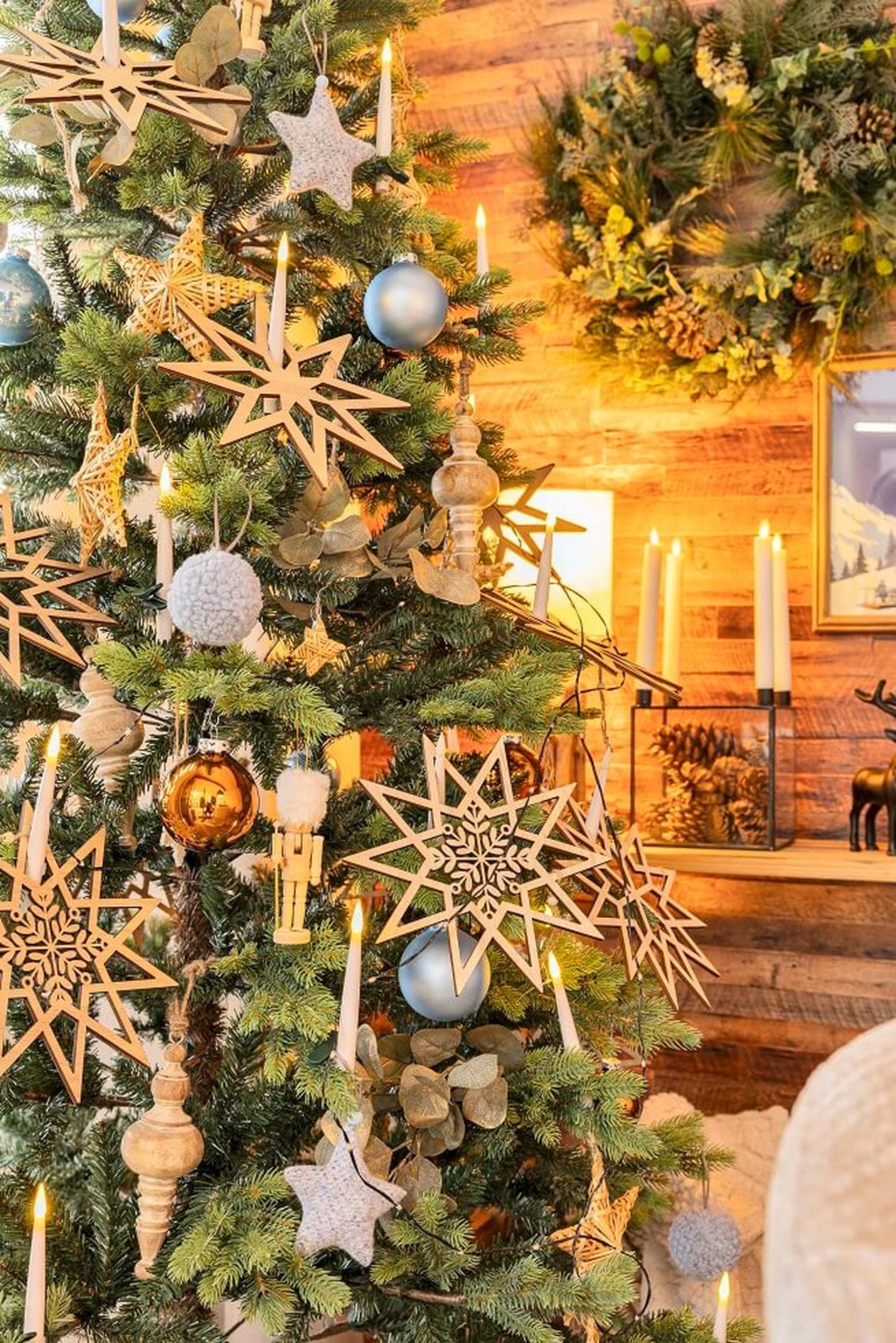 Der Weihnachtsbaum ist mit großen hölzernen Sternornamenten, goldenen Kugeln, Kerzen und Tannenzapfen geschmückt und sorgt für eine festliche und gemütliche Atmosphäre.