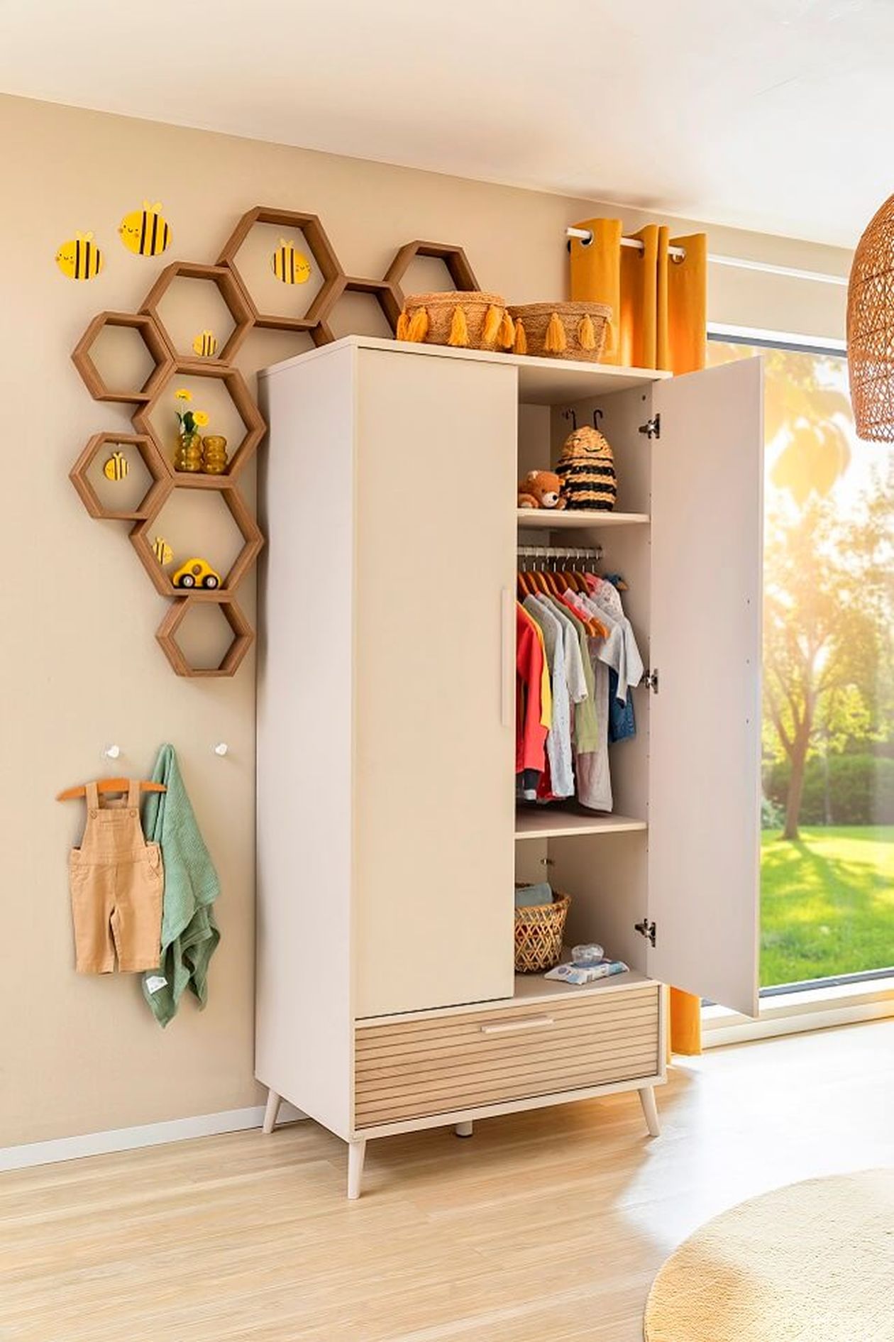 Baby-Kleiderschrank in Beige- und Holztönen neben einem Fenster mit Gartenblick.