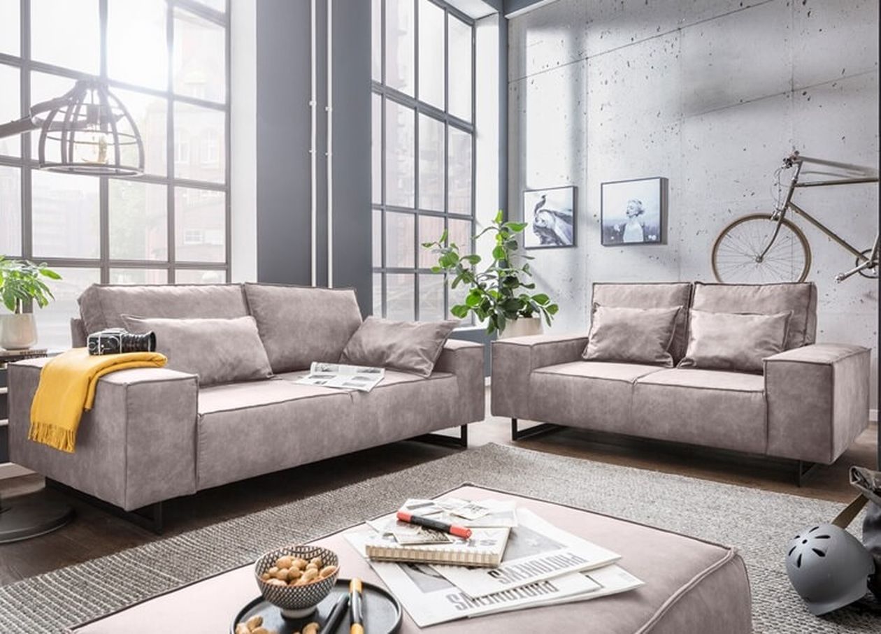 Modernes Wohnzimmer mit zwei grauen Sofas, einem großen Fenster, einem Fahrrad an der Wand und einem Couchtisch mit Zeitschriften und einer Schale Nüsse.