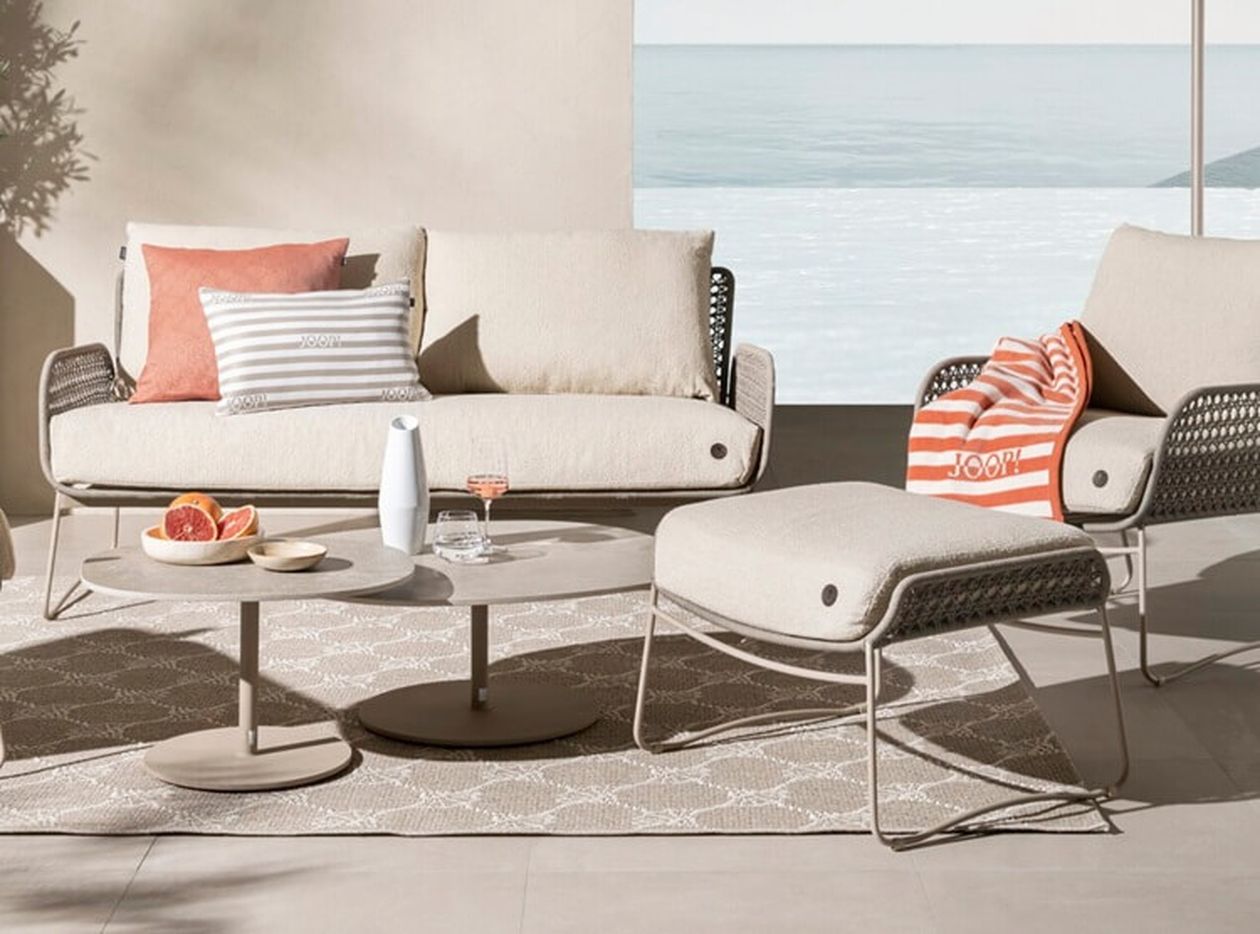 Moderne Außenterrasse mit beigen Möbeln, gestreiften Kissen, einem kleinen Tisch mit Grapefruit und einem Getränk und Blick auf den ruhigen Ozean.