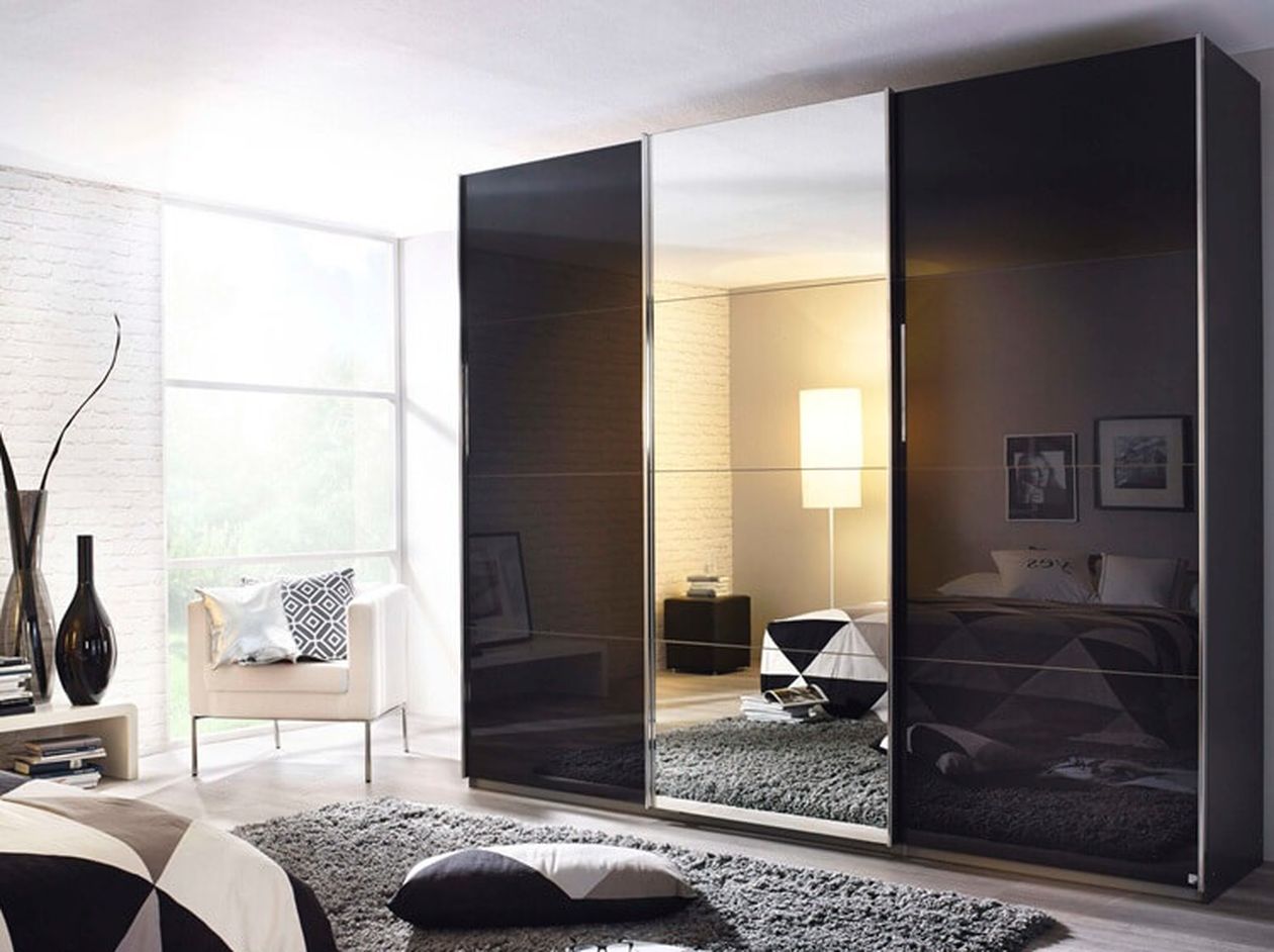 Dreitüriger Schwebetürenschrank in Schwarz Hochglanz mit mittlerer Spiegeltür in einem hellen Schlafzimmer mit schwarz-weißer Dekoration.