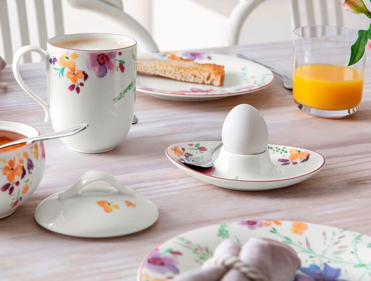 Ein Frühstückstisch mit einem weichgekochten Ei in einem Eierbecher mit Blumenmuster, Toast, Orangensaft und einer Tasse mit Blumenmuster.