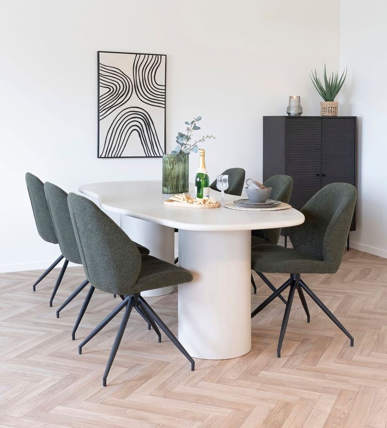 Weißer ovaler Esstisch mit zwei zylindrischen Säulenbeinen, umgeben von sechs dunkelgrünen Bouclé-Stühlen mit schwarzen Spinnenbeinen in einem modernen Esszimmer mit Fischgrätparkett.