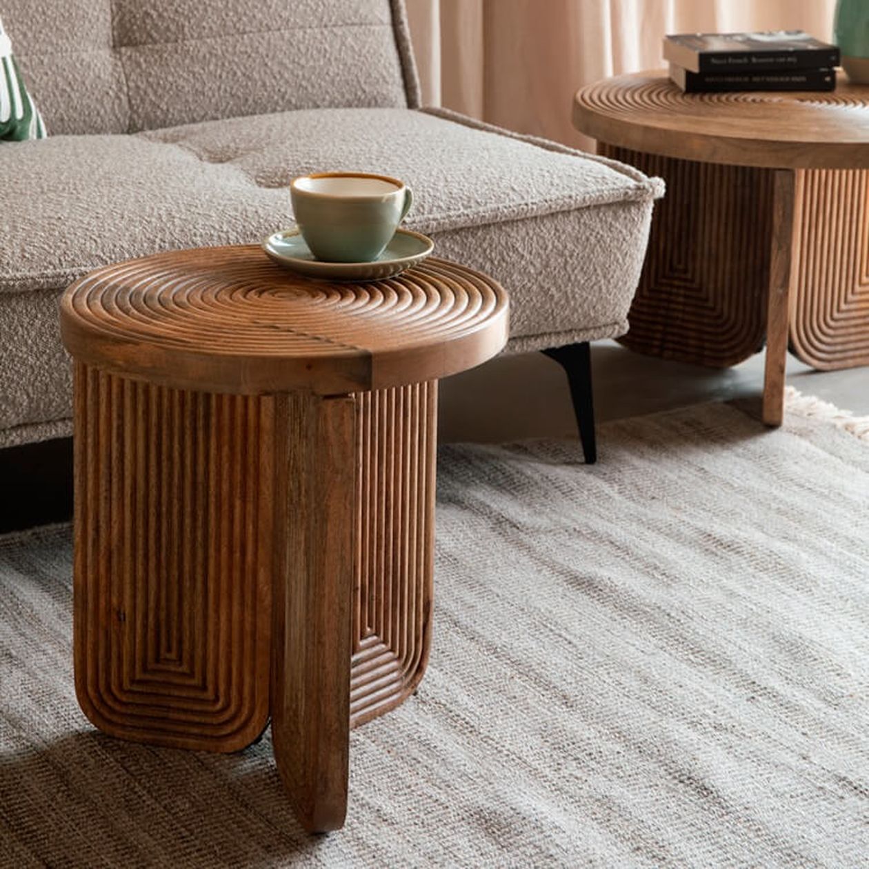 Runder Beistelltisch aus dunklem Holz mit konzentrischen Rillen auf der Oberfläche und geriffelten Beinen, darauf eine Tasse, neben einem beigen Bouclé-Sofa.