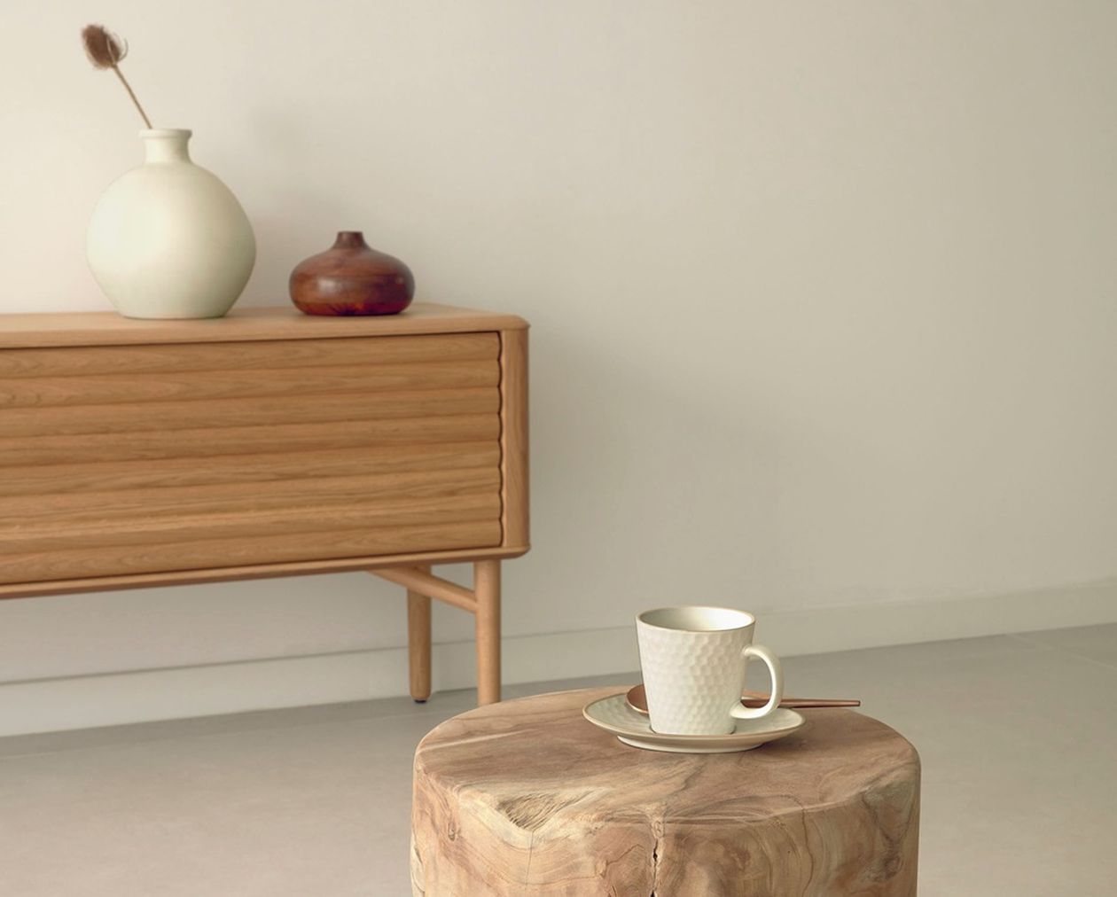 Rustikaler Beistelltisch aus einem massiven Baumstamm mit natürlicher Maserung, darauf eine weiße Tasse mit Untertasse, vor einem Sideboard auf beigem Teppich.