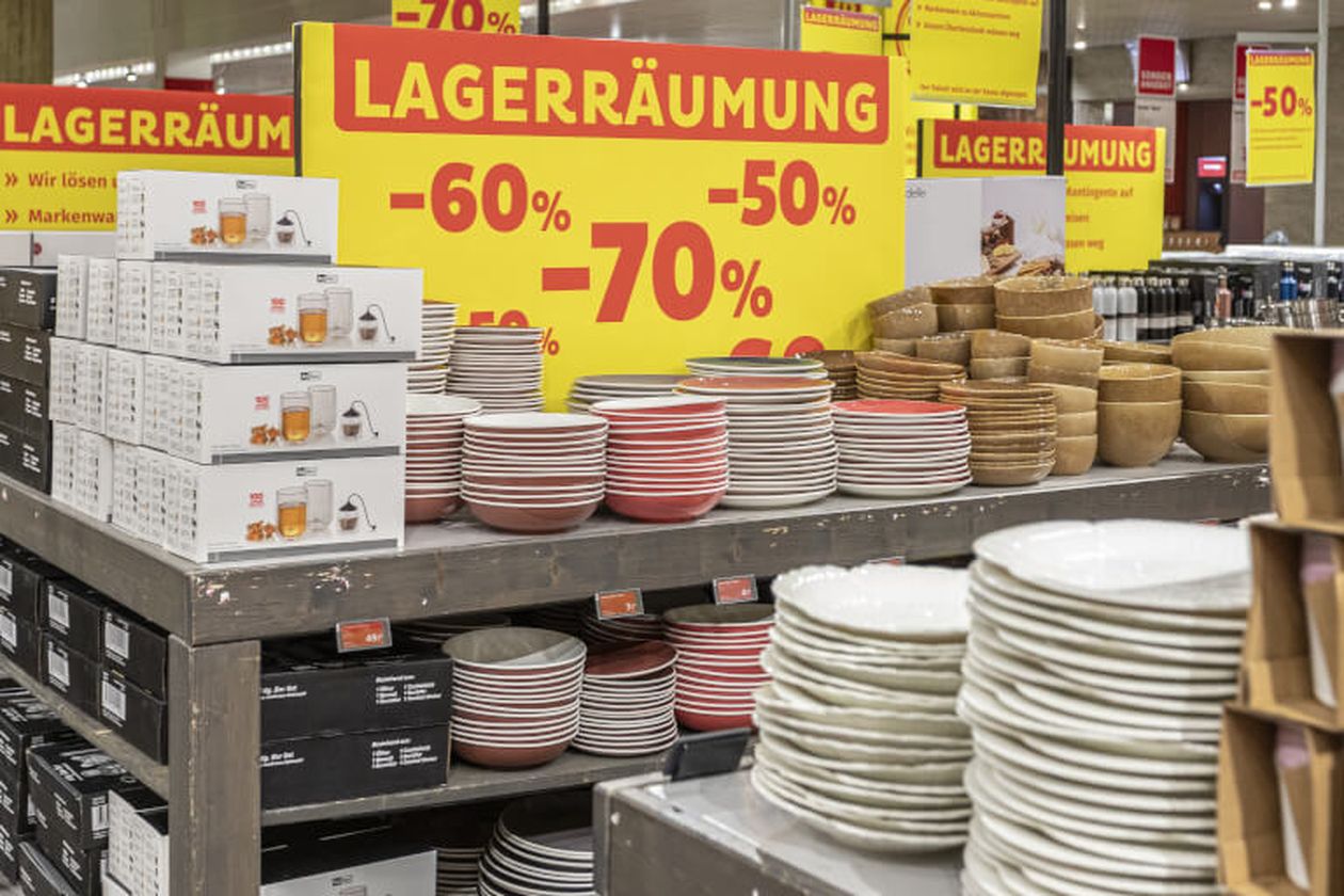 Geschirr im Supermarkt mit großen Rabatten von 50% bis 70%. Gelbe "Lagerräumung"-Schilder, verschiedene Teller und Schüsseln.