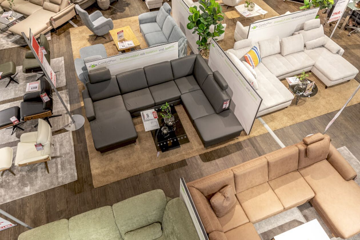 Sofalandschaft in einem Möbelgeschäft, mit verschiedenen Ecksofas in Grau, Beige und Grün auf Teppichen, dekoriert mit Tisch und Pflanzen.
