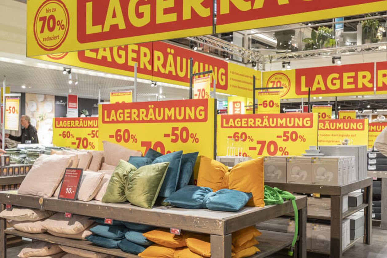 Ein Geschäft mit Lagerverkaufs-Schildern, die Rabatte von 50% bis 70% anzeigen, und Kissen auf einem Tisch.