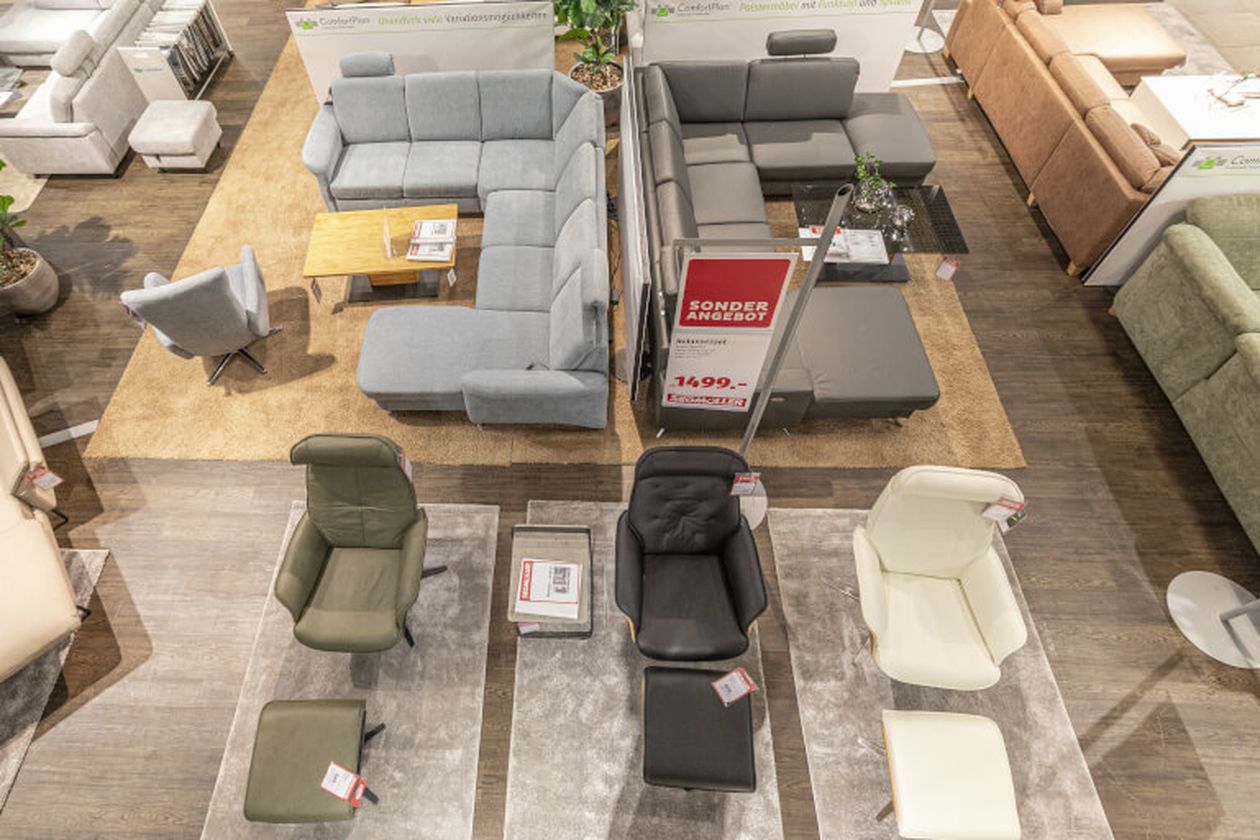 Sofalandschaft in einem Möbelgeschäft, mit verschiedenen Ecksofas in Grau, Beige und Grün auf Teppichen, dekoriert mit Tisch und Pflanzen.
