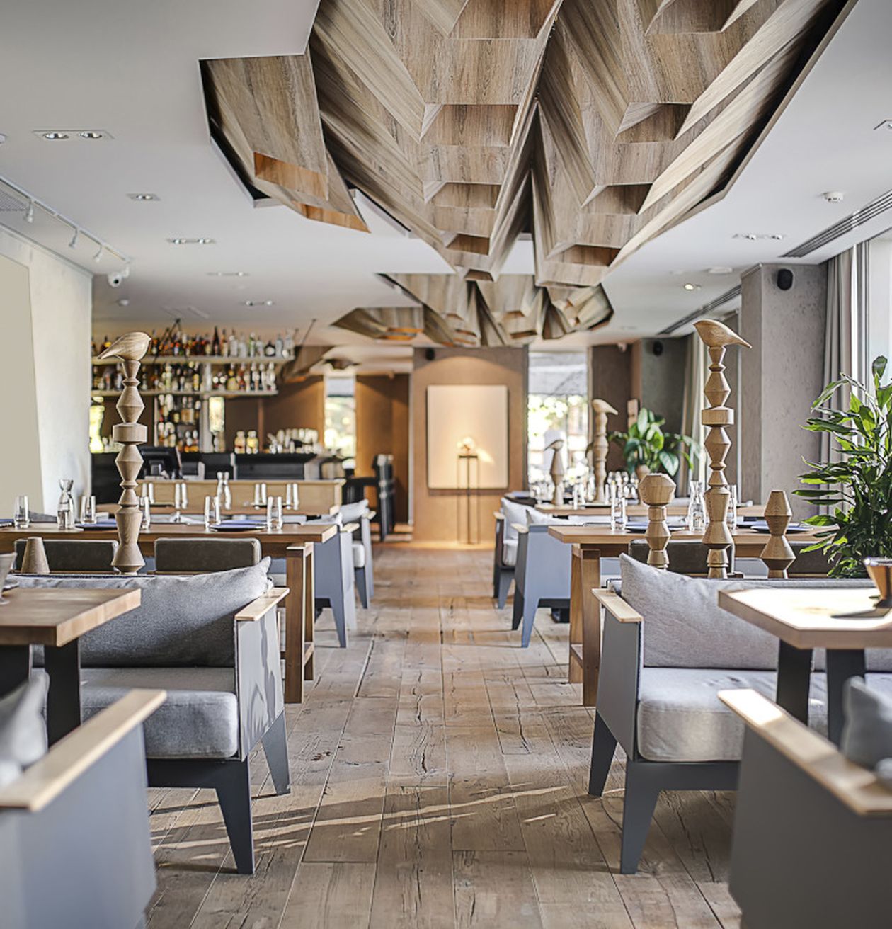 Modern eingerichtetes Restaurant mit Holzdekor, Tischen, Sitzbänken und einer Bar im Hintergrund.
