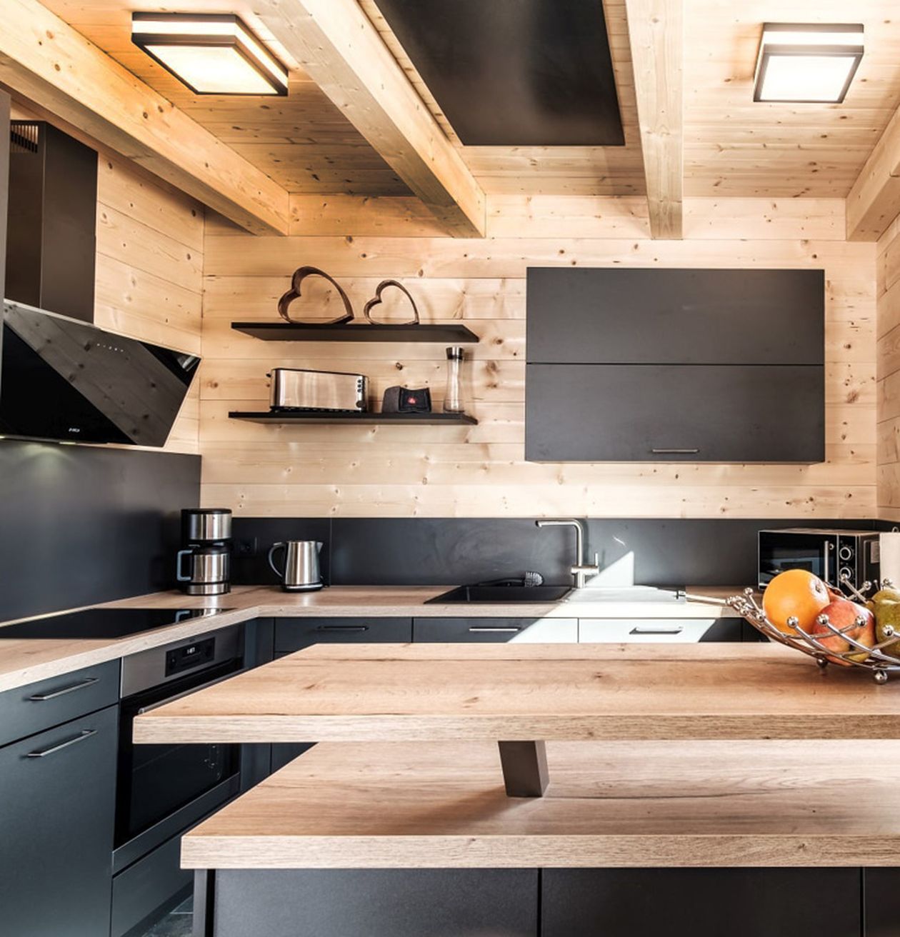 Küche mit Holzdecke und-wänden, schwarzen Schränken und Arbeitsflächen.