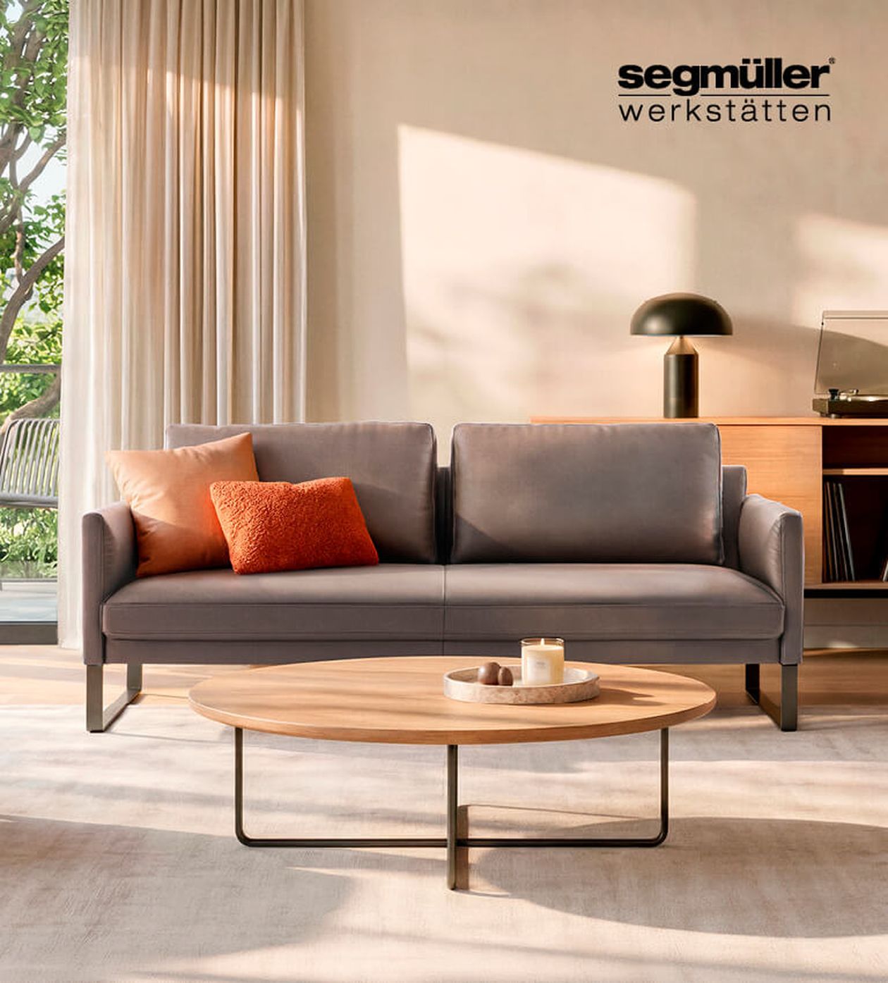 Modernes Wohnzimmer mit grauem Sofa, orangefarbenen Kissen, rundem Holztisch und einer eleganten schwarzen Lampe. Große Fenster und viel Tageslicht durchfluten den Raum.