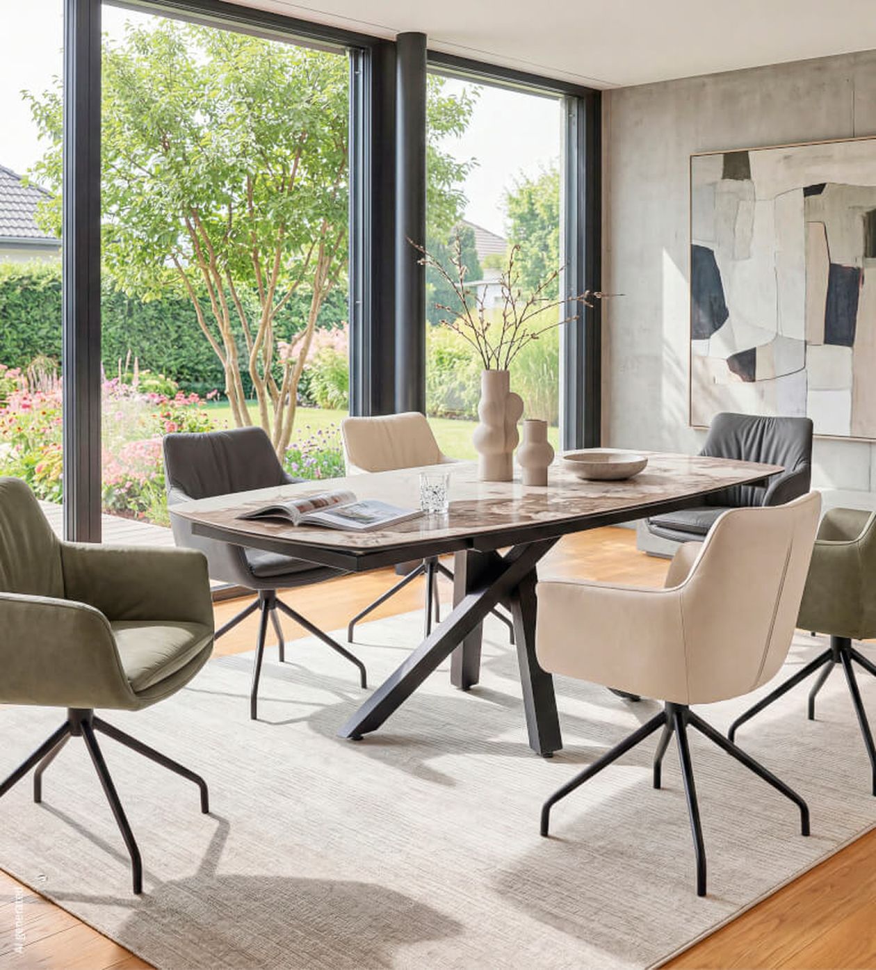 Esszimmer mit großem Tisch, sechs Stühlen, modernen Dekorationen, Kunstwerk an der Wand und großen Fenstern mit Blick ins Grüne.