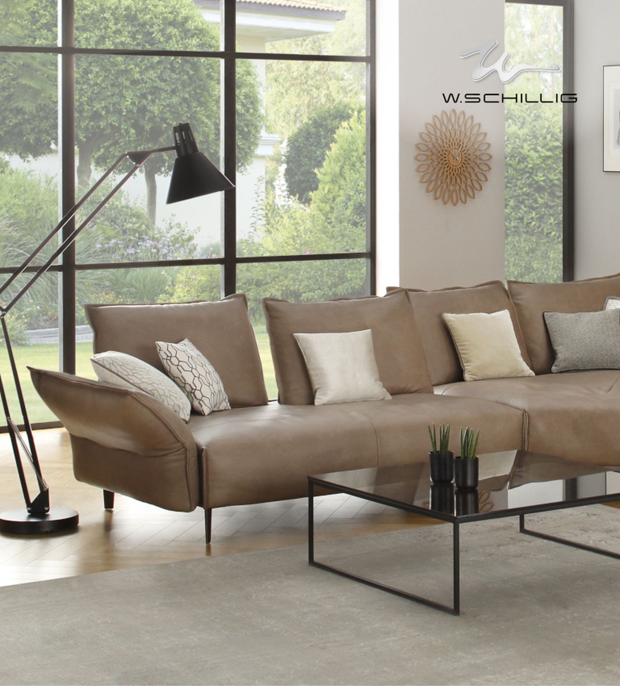 Modernes Wohnzimmer mit braunem Sofa, grauen und weißen Kissen, Glas-Couchtisch und schwarzer Stehlampe. Große Fenster mit Gartenblick.
