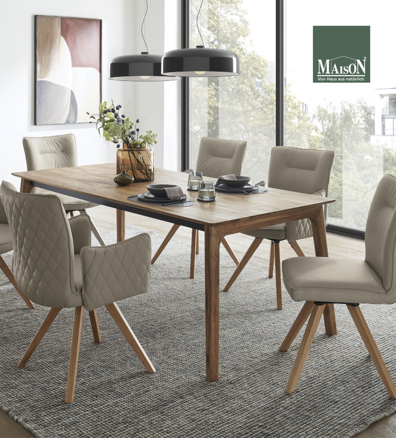 Esszimmer mit Holztisch und gepolsterten Stühlen, modernen Hängeleuchten, einem Teppich und großen Fenstern. Gerahmtes Kunstwerk an der Wand.