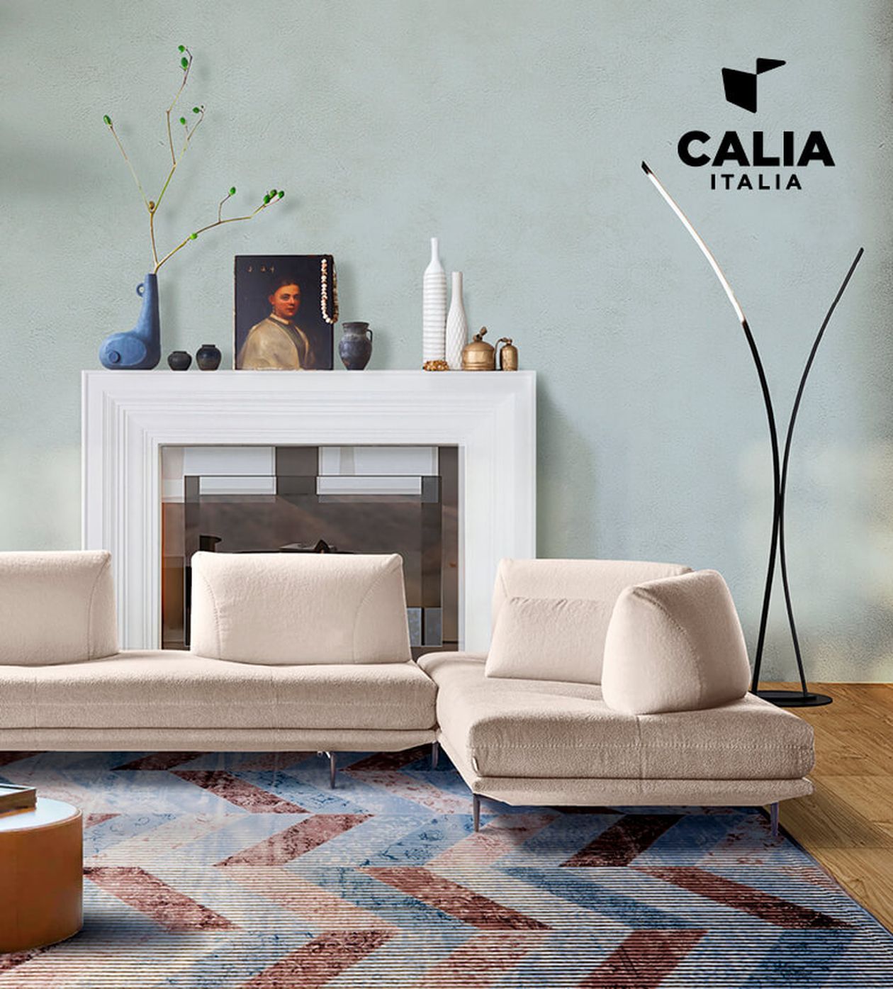 Modernes Wohnzimmer mit beigefarbenem Ecksofa, dekorativen Vasen, einem Porträt auf dem Kaminsims und einer eleganten Stehlampe. Das Logo von „Calia Italia“ ist zu sehen.