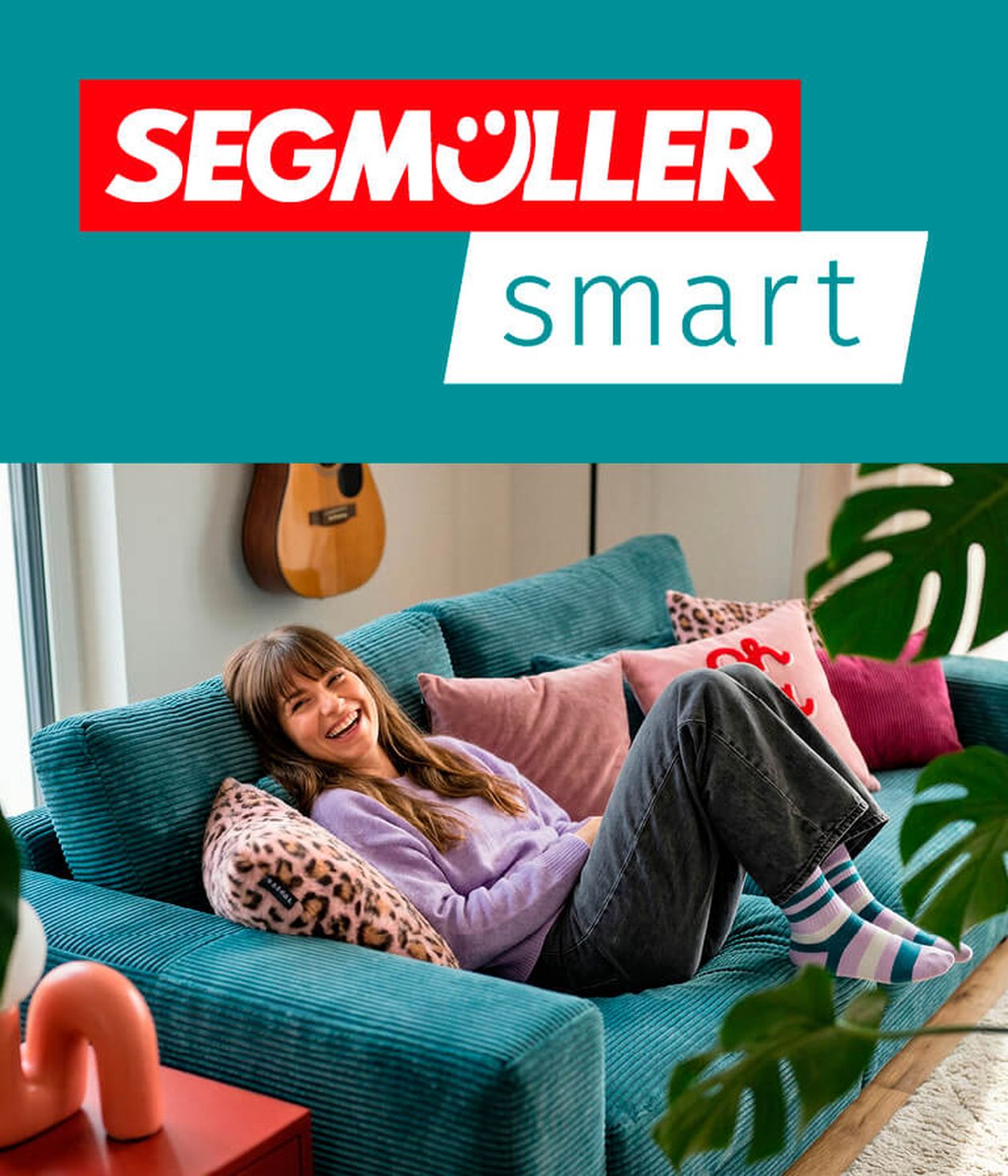Teaser zur Bewerbung von SEGMÜLLER smart: Eine junge Frau in einem lila Pullover und gestreiften Socken lächelt und entspannt auf einem türkisfarbenen Sofa mit bunten Kissen. An der Wand daneben hängt eine Gitarre.