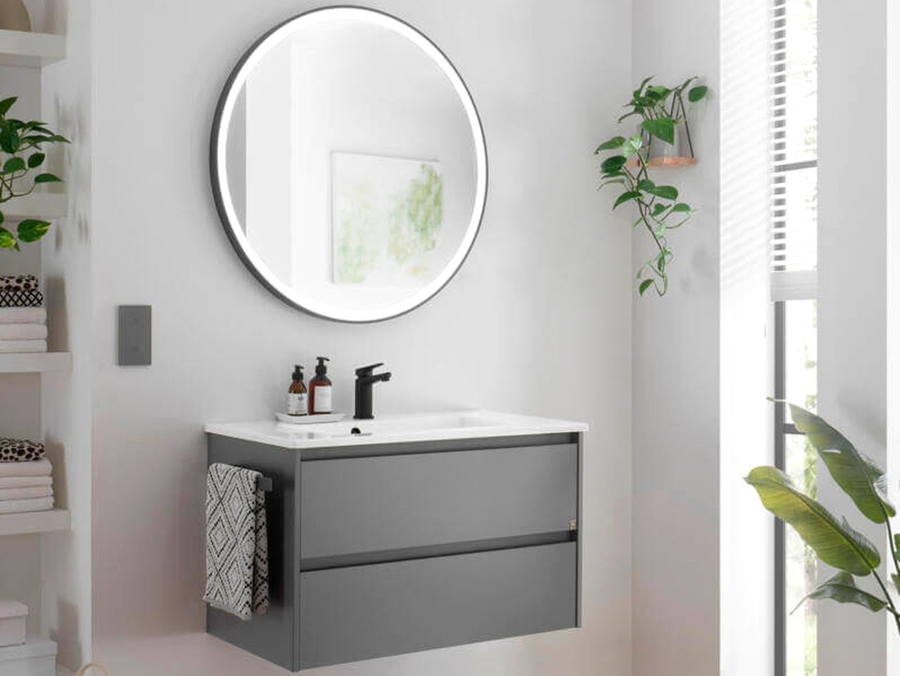 Modernes Badezimmer mit rundem Spiegel, grauem Waschtisch, schwarzem Wasserhahn und Hängepflanzen. Natürliches Licht durch das Fenster rechts.