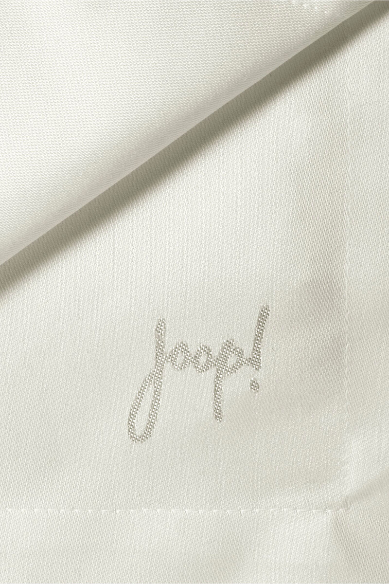 Nahaufnahme eines weißen Stoffes mit dem mit hellgrauem Garn aufgestickten Schriftzug „Joop!“, der die Struktur und die gefalteten Eckdetails zeigt.