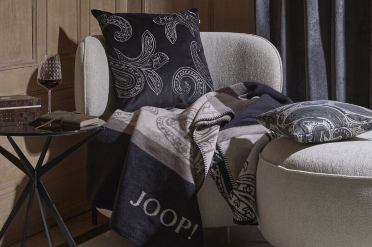 Produktbild: Kissenbezüge der Marke JOOP! auf einem Sofa in einem dunkel gehaltenen Wohnzimmer.