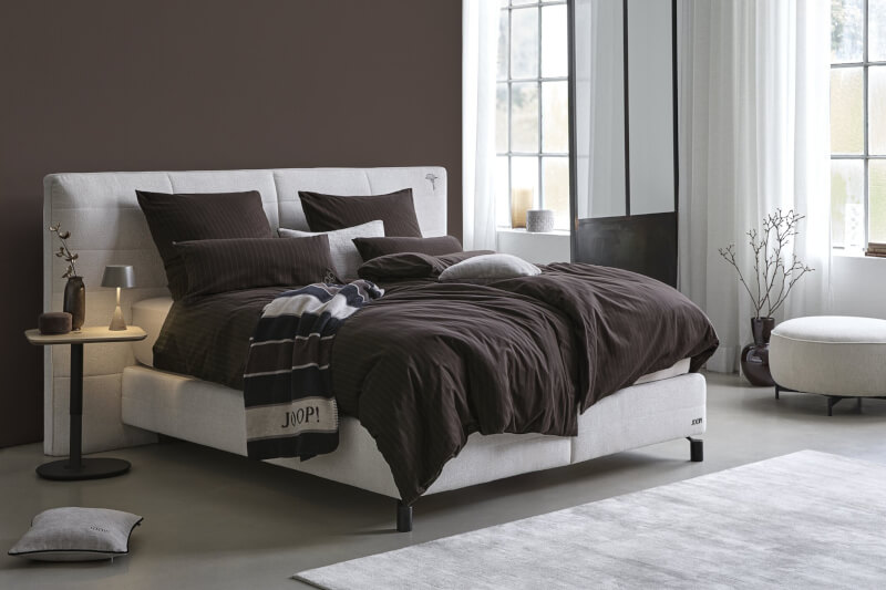 Produktbild: Gestreifte Bettwäsche der Marke JOOP! auf einem Bett in einem braunen Schlafzimmer.