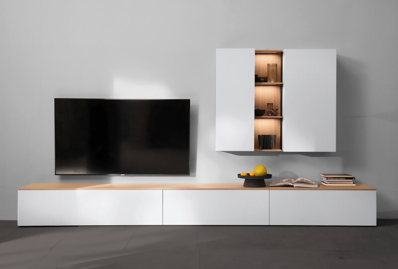Modernes Wohnzimmer mit einem an der Wand montierten Flachbildfernseher, weißen Schränken, Holzregalen und Dekorationsgegenständen auf einer Holzoberfläche.