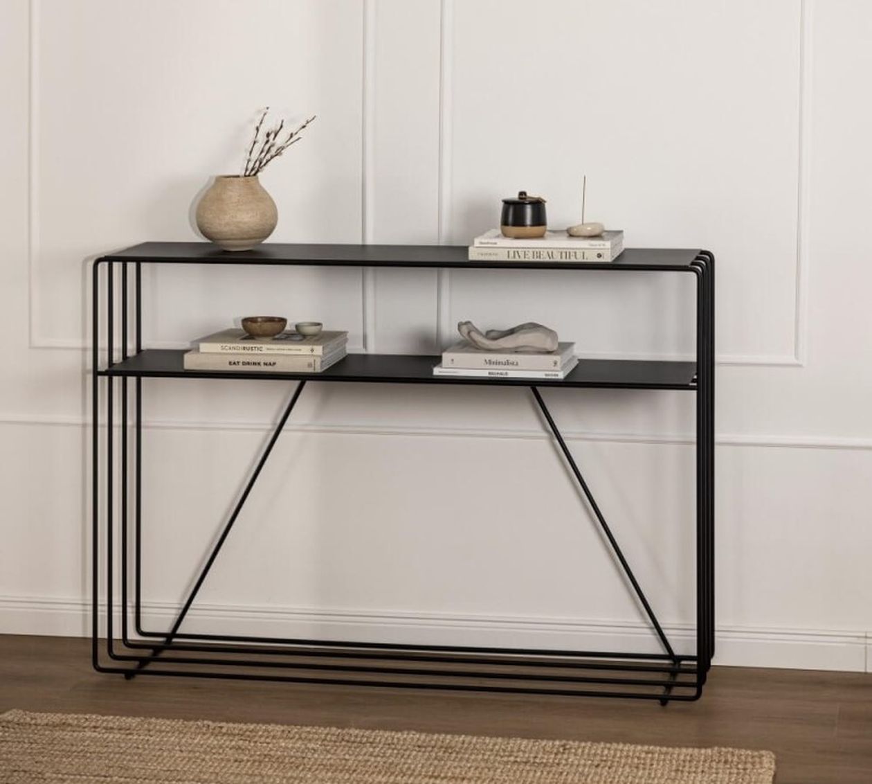Schwarze Metall-Konsole Ria, dekoriert mit Büchern, einer kleinen Vase und minimalistischen Ornamenten.