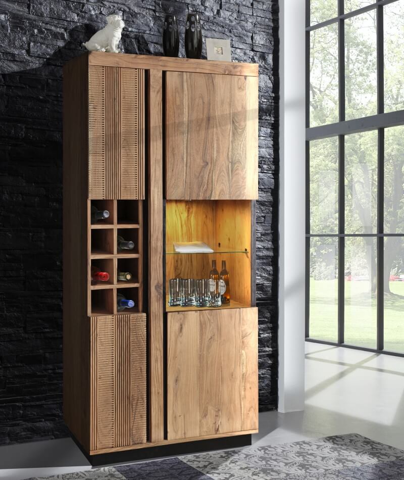 Holzschrank mit Weinfach und dekorativen Gegenständen obendrauf, vor einer dunklen Ziegelwand nahe einem großen Fenster.