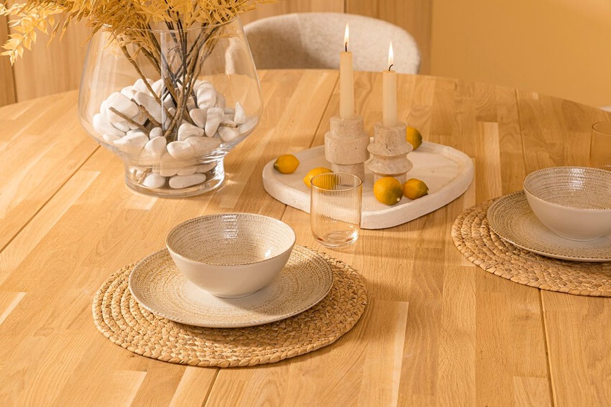 Holztisch mit Tellern auf runden Platzsets, Trockenblumen in einer Vase, brennenden Kerzen auf einem Tablett und Zitronen als Dekoration.