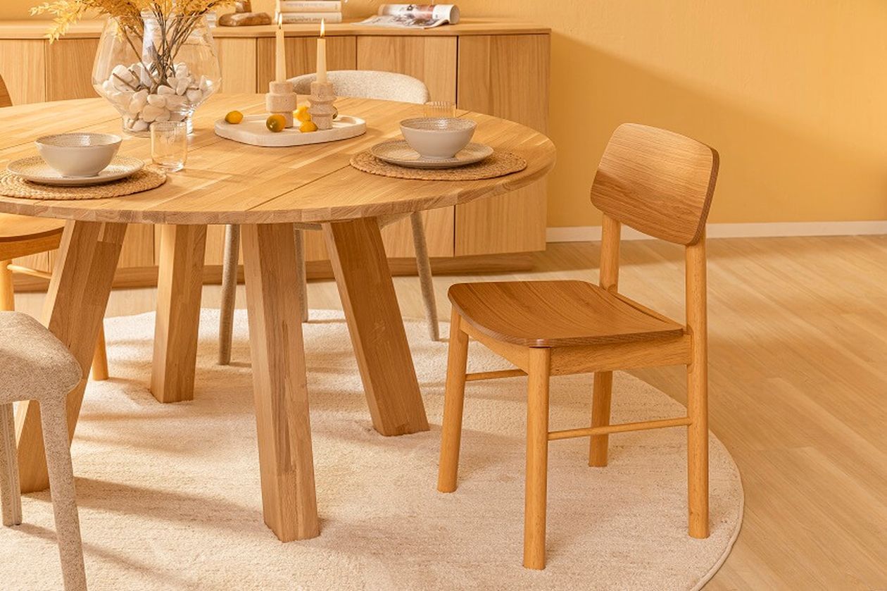 Ein gemütliches Esszimmer mit einem runden Holztisch, gepolsterten Stühlen, Kerzen und Geschirr auf Untersetzern, in warmen Beigetönen eingerichtet.