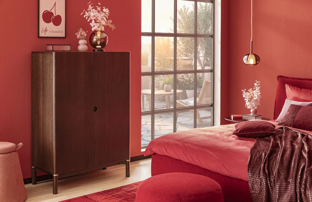 Rotes Schlafzimmer mit modernem Design, Holzmöbeln, dekorativen Pflanzen und einem großen Fenster. Wandposter mit "Life is beautiful"-Text.