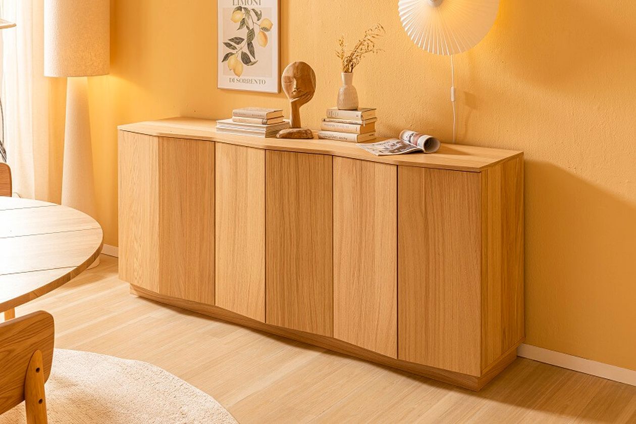 Holzsideboard in hellem Raum, dekoriert mit Büchern, Vasen und Kunstobjekten. An der Wand ein Bild und eine Wandlampe.